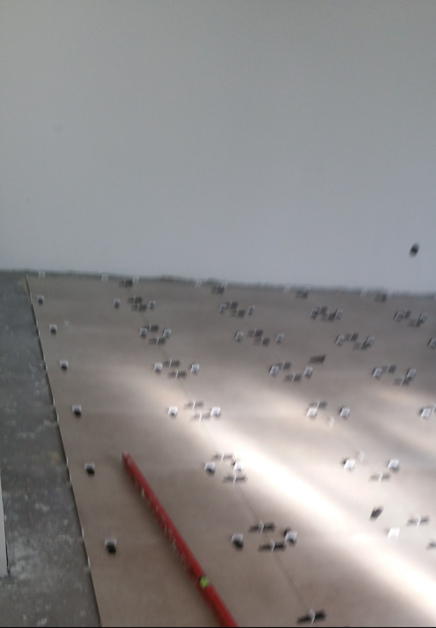 Ułożone płytki podłogowe z krzyżykami dystansowymi i czerwoną poziomicą, przygotowane do fugowania, w pomieszczeniu z szarą ścianą.