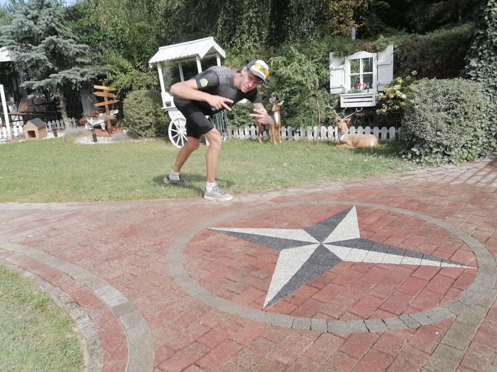 Ozdobna kostka brukowa z motywem gwiazdy na posesji z dekoracjami ogrodowymi i osobą w tle. Czerwona kostka w otoczeniu zieleni.