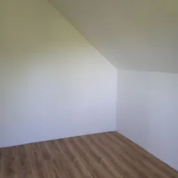 Pomalowane na biało poddasze ze skośnym sufitem i brązowymi panelami podłogowymi. Widok na róg pokoju, sufit i ściany gładkie, jednolite.