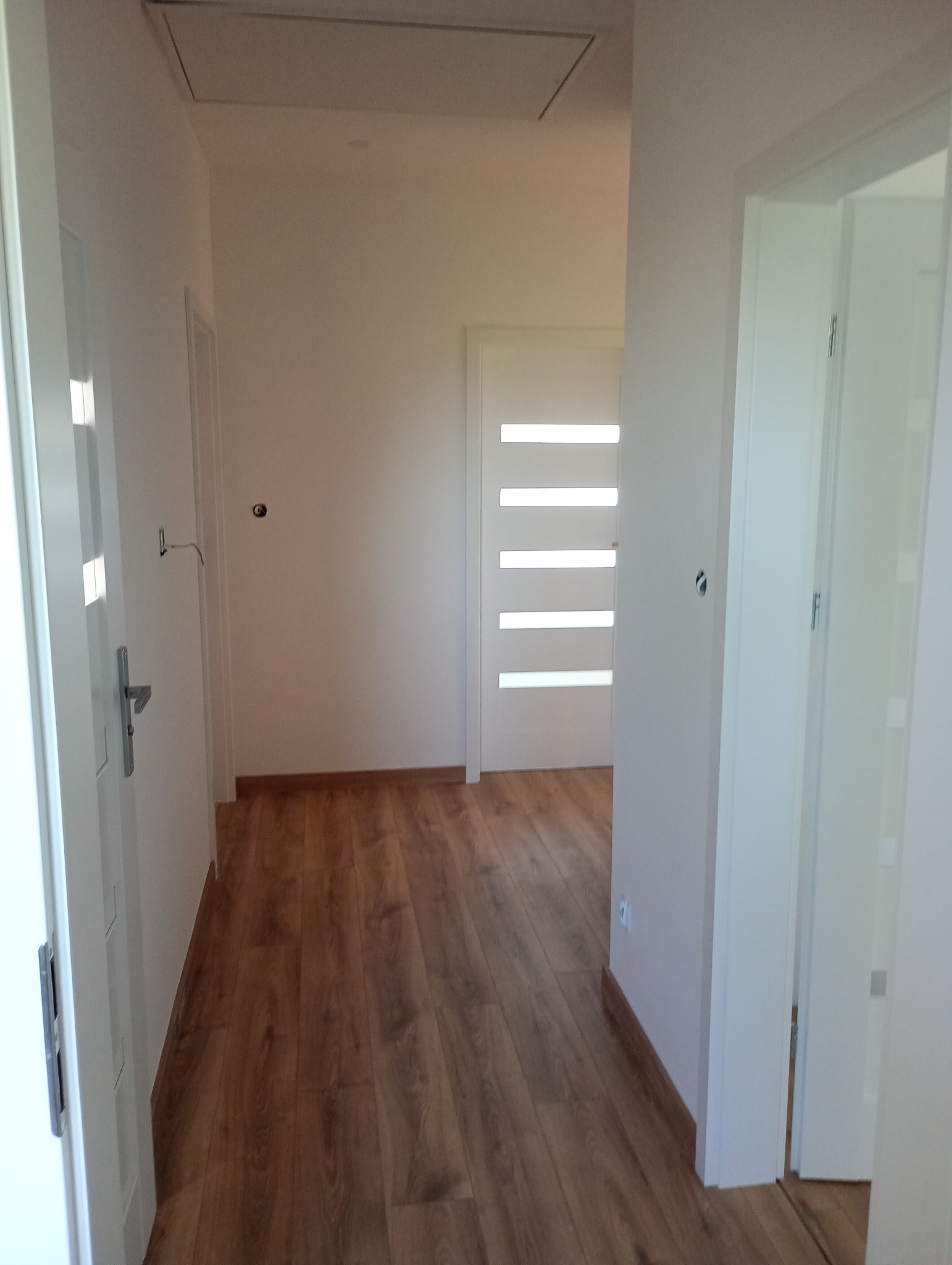 Jasne wnętrze po remoncie: drewniana podłoga, białe ściany i drzwi z poziomymi przeszkleniami. Widoczny fragment sufitu z klapą inspekcyjną.