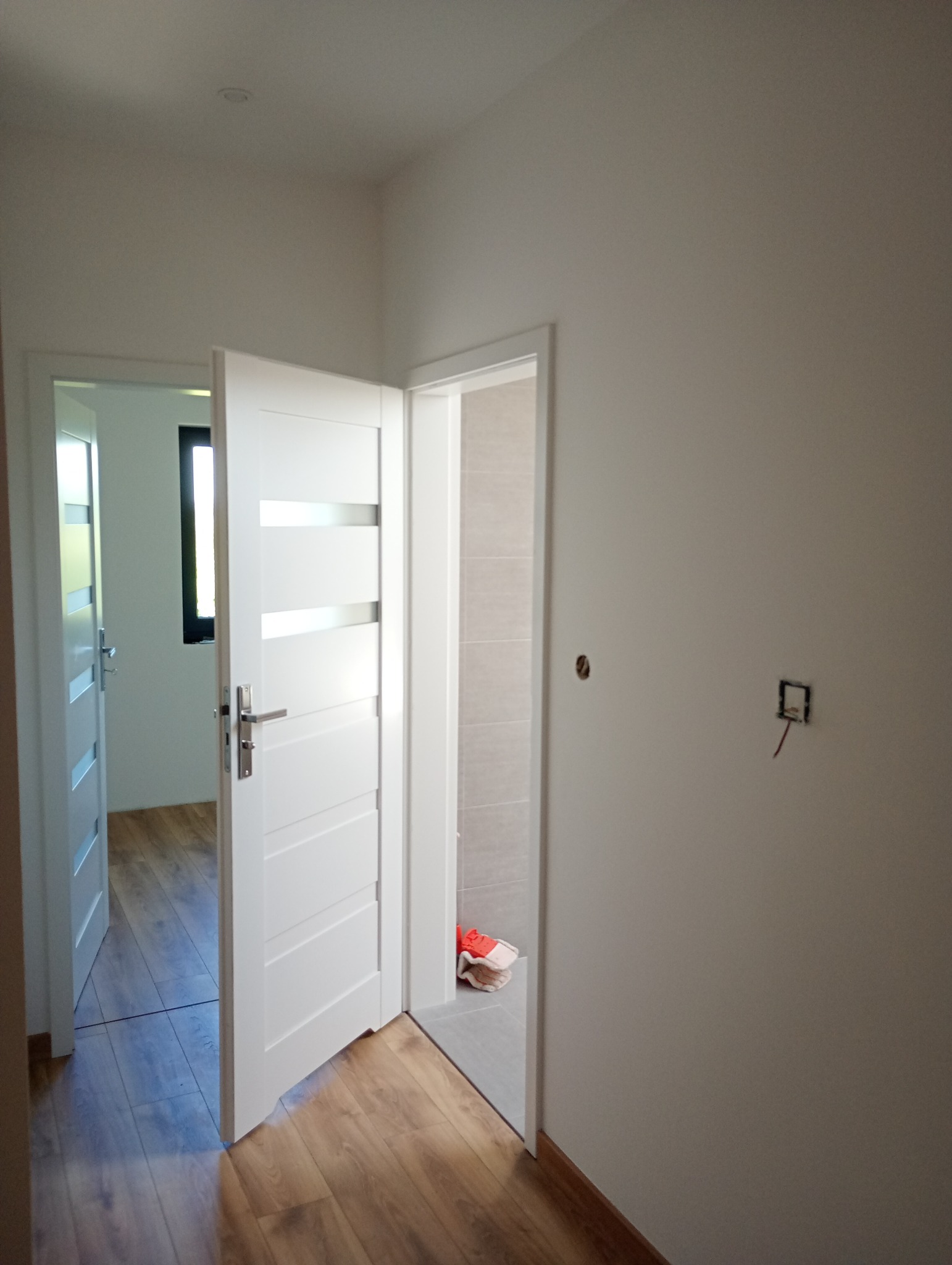 Nowoczesne, białe drzwi wewnętrzne z przeszkleniami, otwarte w wyremontowanym mieszkaniu z drewnianą podłogą i świeżo pomalowanymi ścianami na jasny kolor.