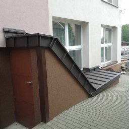 Usługi Ogólnobudowlane - Zabezpieczenie piwnicy budynku mieszkalnego blachą trapezową w kolorze grafitowym, z widocznym wejściem i oknami na elewacji.