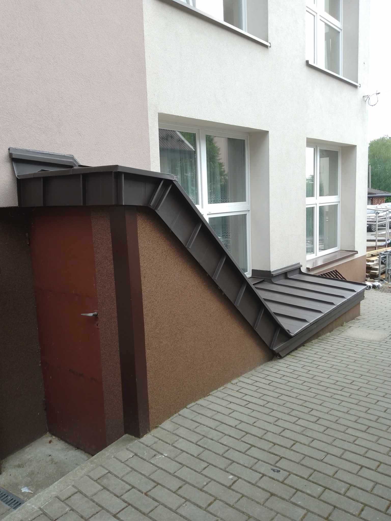Zabezpieczenie piwnicy budynku mieszkalnego blachą trapezową w kolorze grafitowym, z widocznym wejściem i oknami na elewacji.