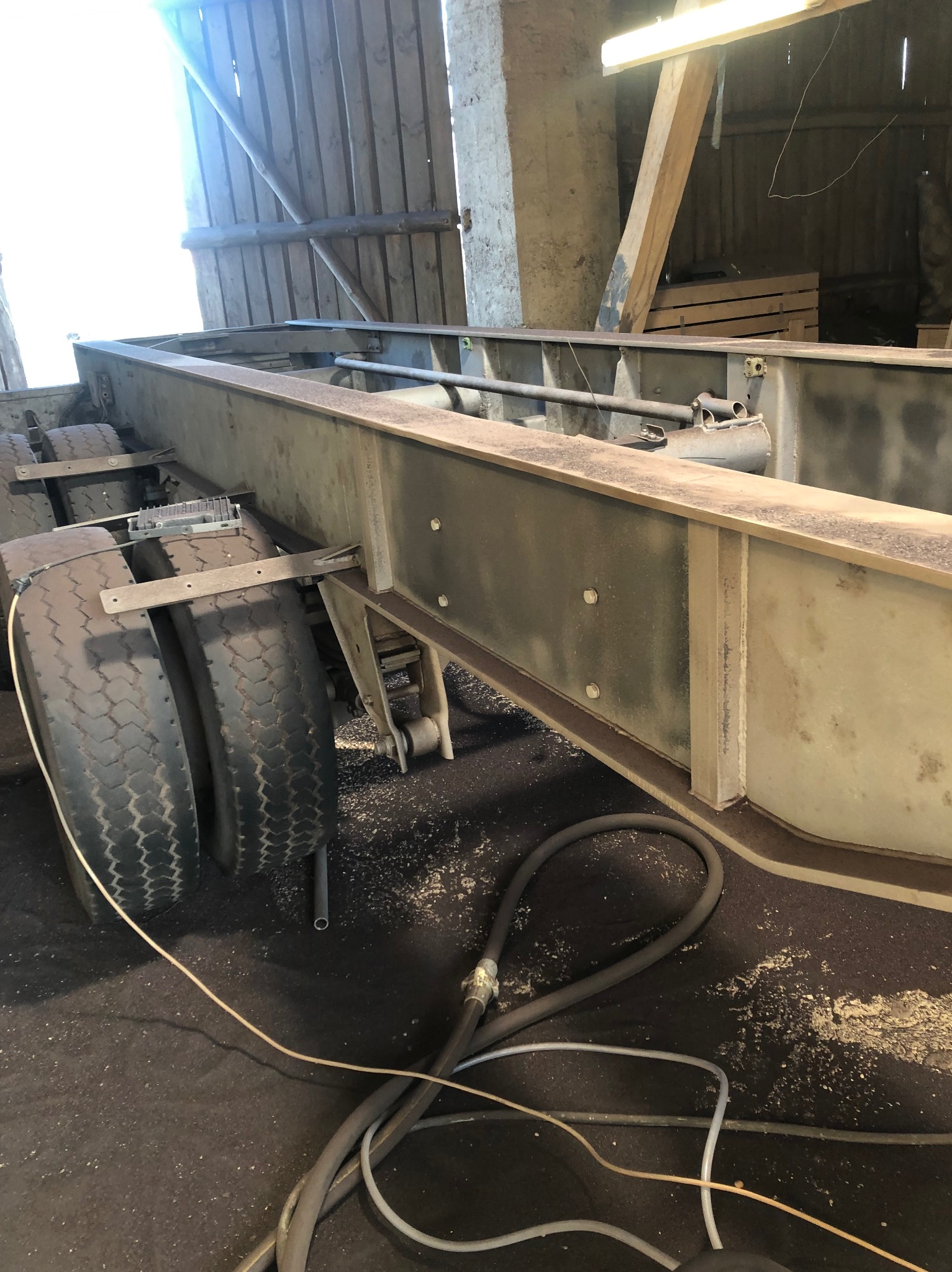 Rama ciężarówki po czyszczeniu, widoczne ślady korozji i resztki starej farby, podłoga warsztatu z przewodami.