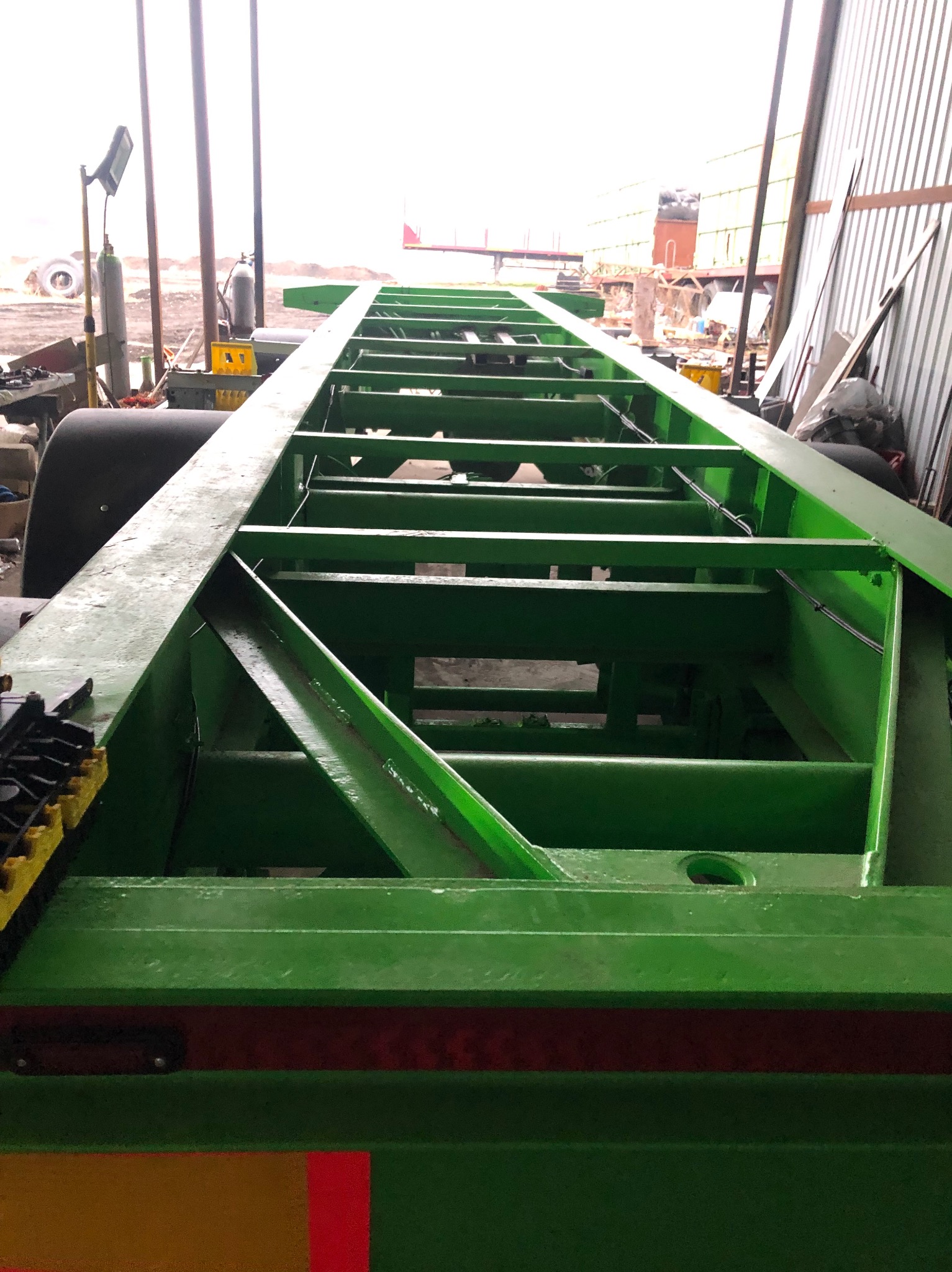 Zielona, metalowa rama przyczepy po piaskowaniu i malowaniu, widoczna struktura kratowa i spawane łączenia, w tle warsztat.