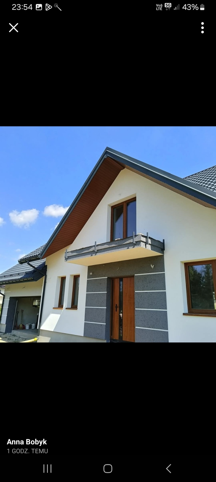 Elewacja domu jednorodzinnego z dekoracyjnym tynkiem w odcieniach szarości i bieli, widok na wejście główne i fragment garażu, błękitne niebo w tle.