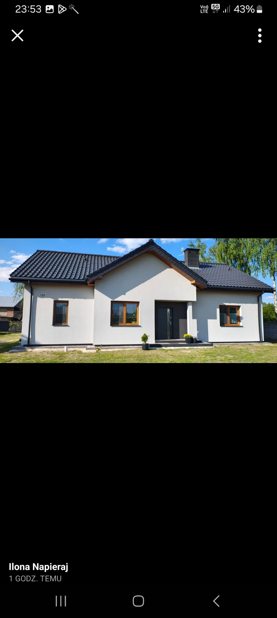 Biały dom z ciemną dachówką i drewnianymi oknami, numer 12A na elewacji. Widoczny komin i fragment zieleni. Dom po remoncie elewacji.