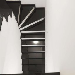 ZAKŁAD OBRÓBKI KAMIENIA NATURALNEGO RSGranit ROMANA JANKOWSKA - Nowoczesne, czarne schody z białymi akcentami, widok z góry, minimalistyczny design, polerowana powierzchnia odbija światło.