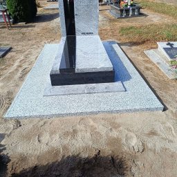 ZAKŁAD OBRÓBKI KAMIENIA NATURALNEGO RSGranit ROMANA JANKOWSKA - Granitowy pomnik nagrobny z czarnym akcentem i napisem 'Ave Maria' na cmentarzu, widoczne ślady stóp na piasku wokół.