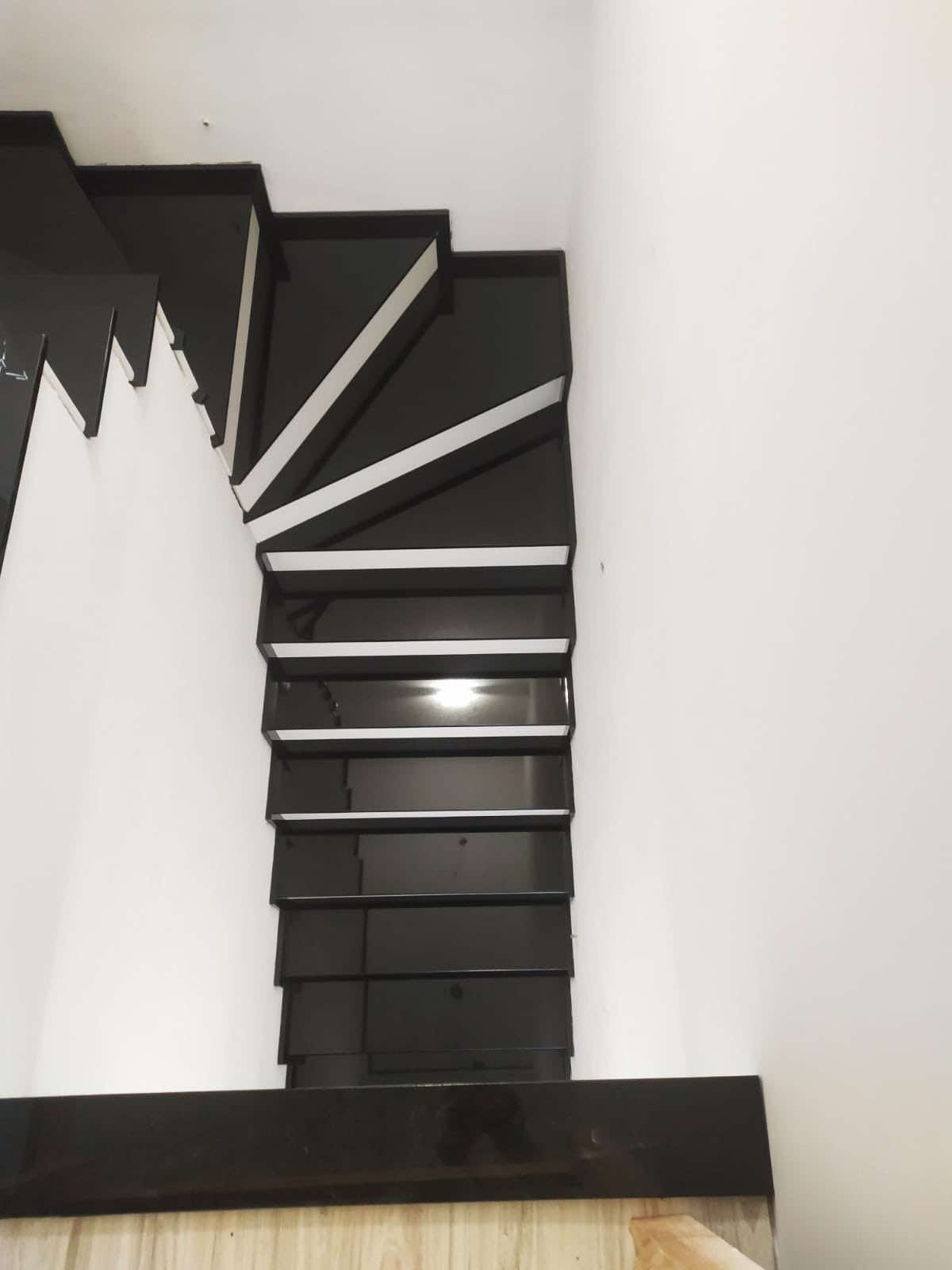 Nowoczesne, czarne schody z białymi akcentami, widok z góry, minimalistyczny design, polerowana powierzchnia odbija światło.