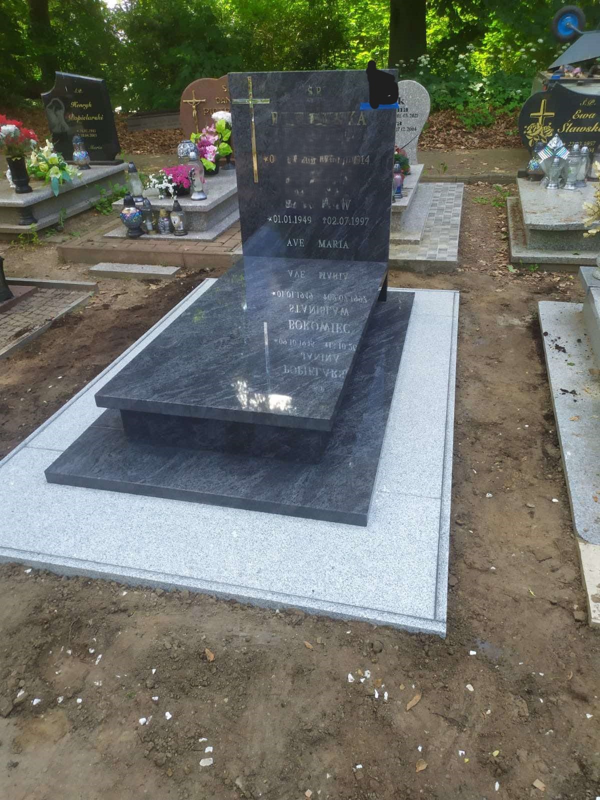 Nowoczesny, ciemnoszary pomnik z jasnoszarą podstawą na cmentarzu, odbicie nieba na polerowanej powierzchni płyty nagrobnej.