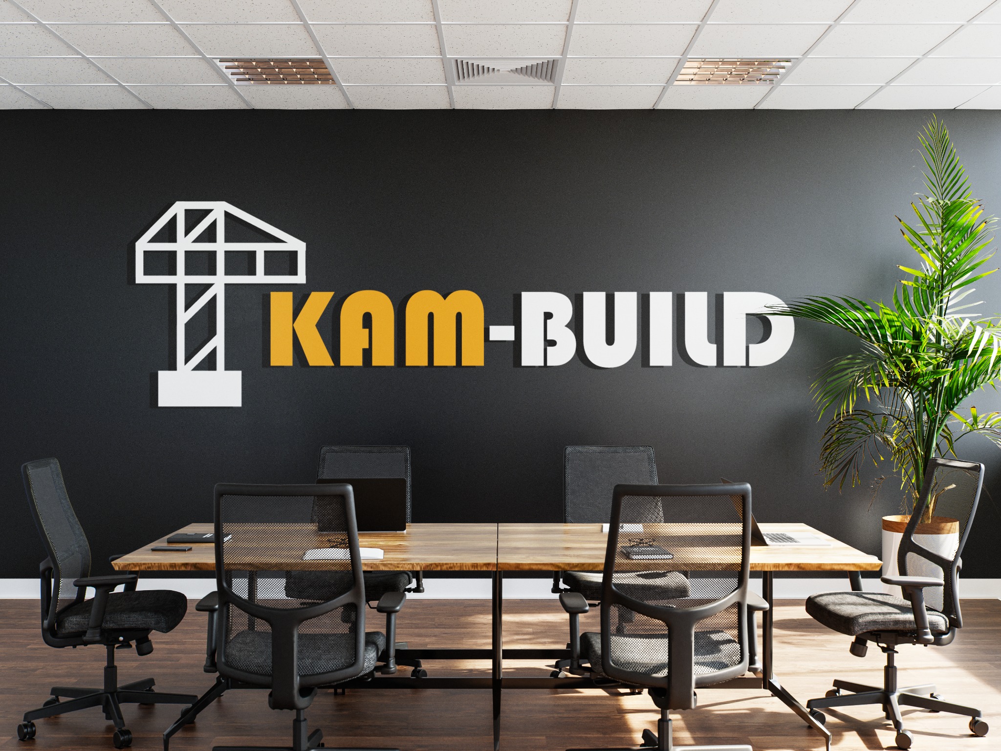 Logo firmy KAM-BUILD z symbolem dźwigu na czarnej ścianie biura, widoczny stół konferencyjny z laptopami i krzesłami biurowymi, roślina doniczkowa w prawym rogu.