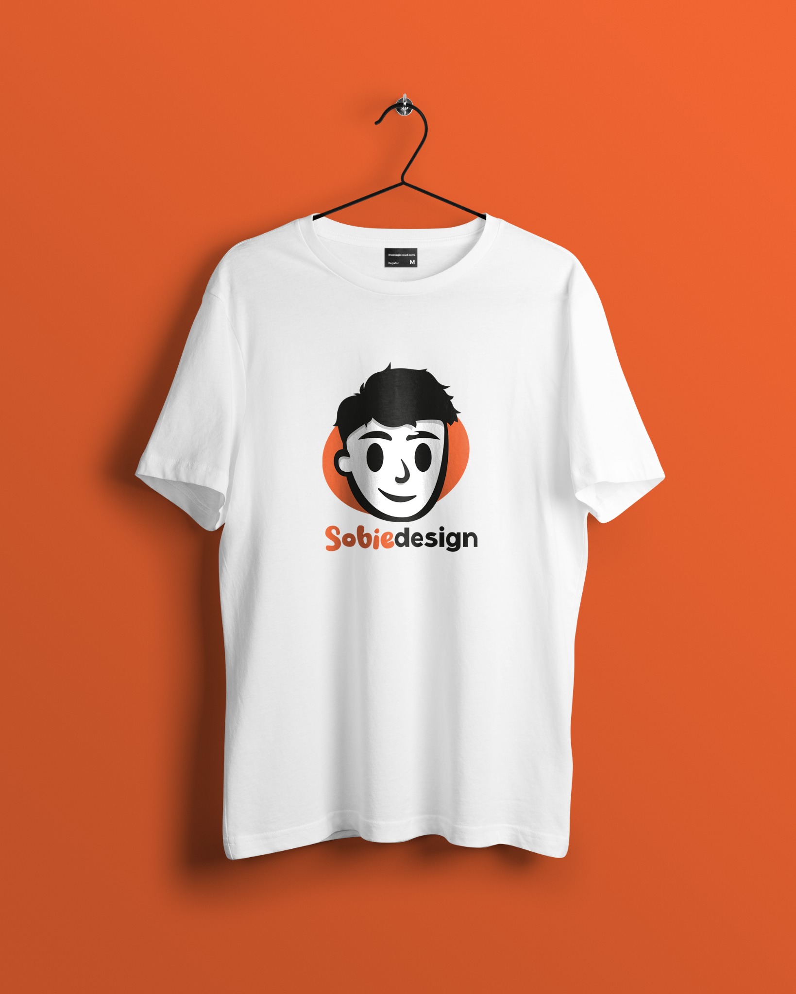 Biała koszulka z czarnym logo stylizowanym na portret i pomarańczowym akcentem, wisząca na wieszaku na tle pomarańczowej ściany.