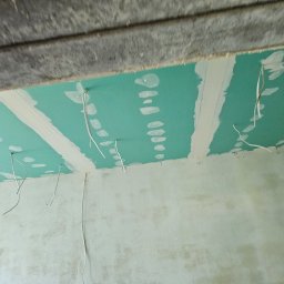 BART-BUD BARTOSZ ŁOŚ WYKOŃCZENIA WNĘTRZ - Zielona płyta GK zamontowana na suficie z wystającymi przewodami, przygotowana do dalszych prac wykończeniowych. Widoczne łączenia płyt i surowa ściana.