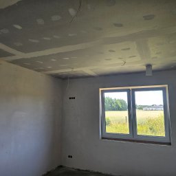BART-BUD BARTOSZ ŁOŚ WYKOŃCZENIA WNĘTRZ - Surowy pokój w trakcie prac wykończeniowych: ściany z gładzią, sufit z płyt karton-gips, okno z widokiem na zieleń. Widoczne oznaczenia na ścianach.