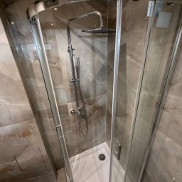 BART-BUD BARTOSZ ŁOŚ WYKOŃCZENIA WNĘTRZ - Nowoczesna kabina prysznicowa z chromowanymi elementami i deszczownicą, wykończona płytkami imitującymi marmur. Widoczny fragment toalety. Górny kadr.