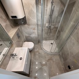 BART-BUD BARTOSZ ŁOŚ WYKOŃCZENIA WNĘTRZ - Wykończona łazienka z kabiną prysznicową, umywalką i toaletą, wyłożona płytkami imitującymi marmur. Widoczny bojler elektryczny. Ujęcie z góry, podkreślające przestrzeń.