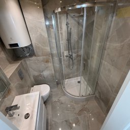 BART-BUD BARTOSZ ŁOŚ WYKOŃCZENIA WNĘTRZ - Wykończona łazienka z kabiną prysznicową, umywalką i toaletą. Płytki imitujące marmur na ścianach i podłodze. Widoczny bojler elektryczny. Nowoczesny design.