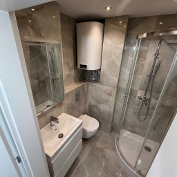 BART-BUD BARTOSZ ŁOŚ WYKOŃCZENIA WNĘTRZ - Wykończona łazienka w beżowych płytkach imitujących marmur. Kabina prysznicowa, umywalka z szafką, toaleta i bojler elektryczny. Oświetlenie punktowe.