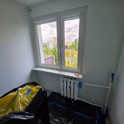 BART-BUD BARTOSZ ŁOŚ WYKOŃCZENIA WNĘTRZ - Świeżo pomalowany pokój z białymi ścianami, oknem PCV, żeliwnym grzejnikiem, niebieską taśmą malarską i folią ochronną na podłodze, z widokiem na osiedle. Widoczny nóż na parapecie.