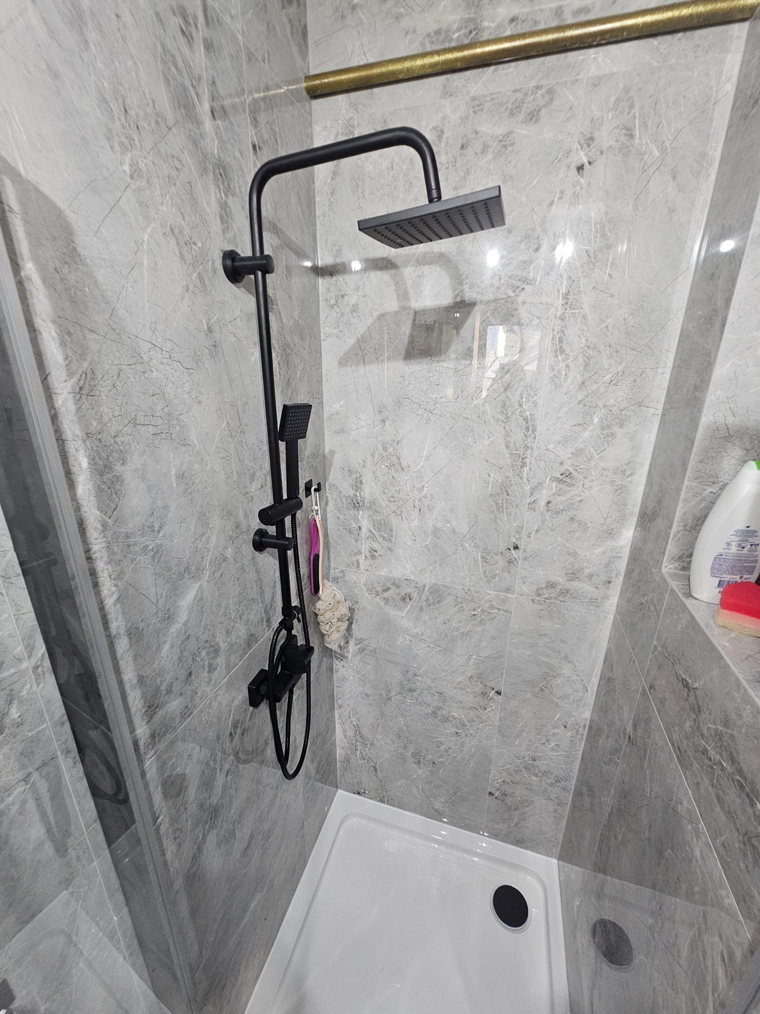 Wykończona kabina prysznicowa z czarną armaturą i szarą marmurową okładziną w Gorzowie Wielkopolskim. Widoczny brodzik i półka z kosmetykami.