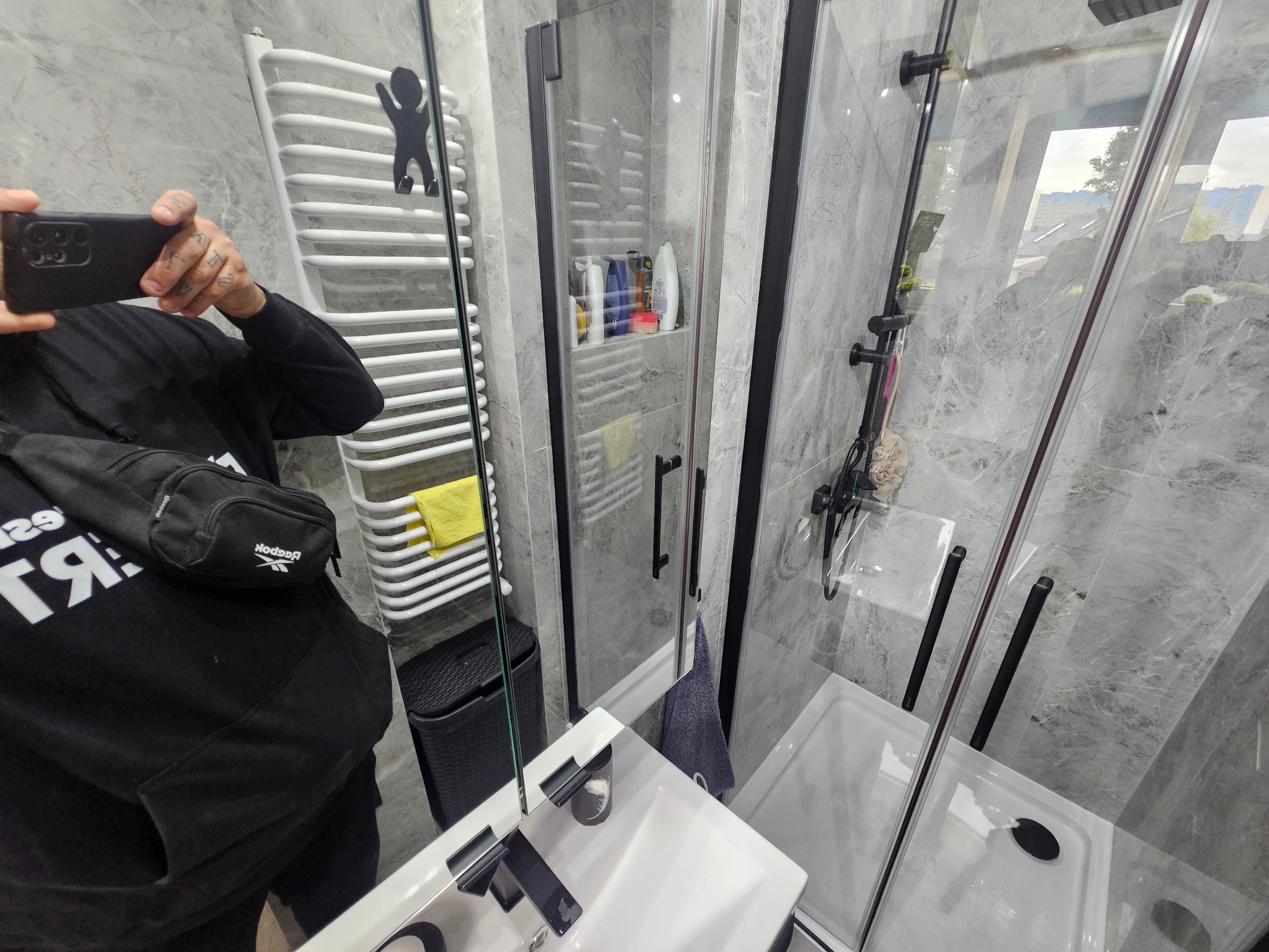 Nowoczesna łazienka z marmurową okładziną, kabiną prysznicową z czarnymi ramami i białym grzejnikiem drabinkowym z wieszakiem.