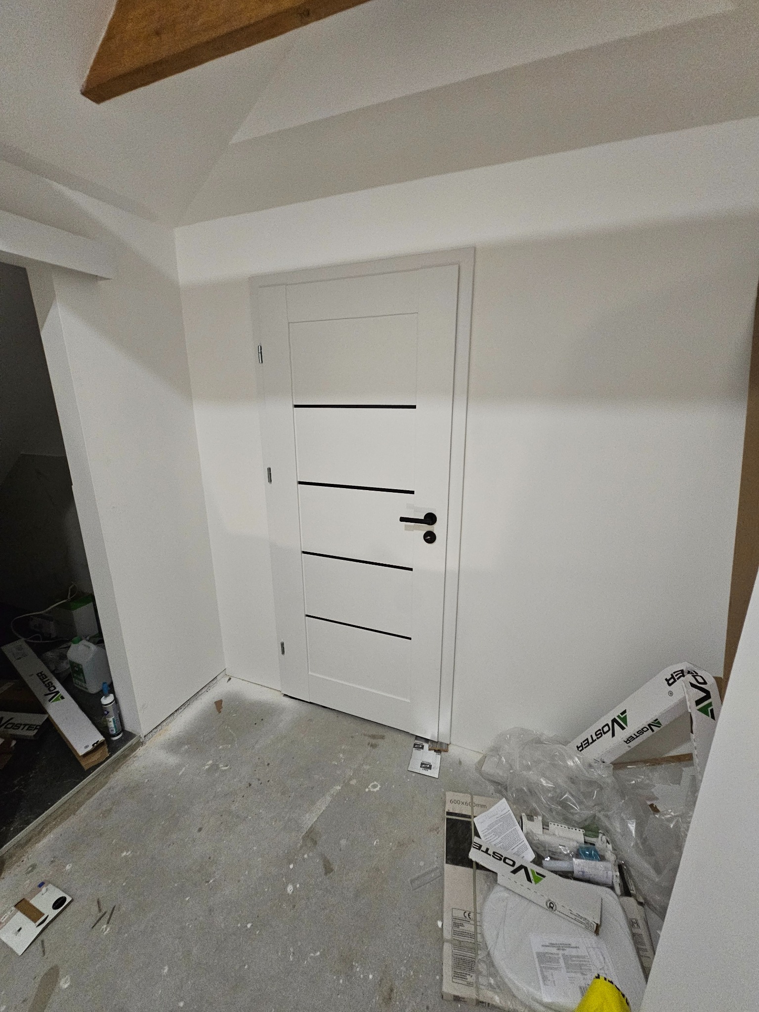 Białe drzwi wewnętrzne z czarnymi poziomymi paskami w nowym domu w Gorzowie Wielkopolskim. Widoczne ślady prac wykończeniowych na podłodze.