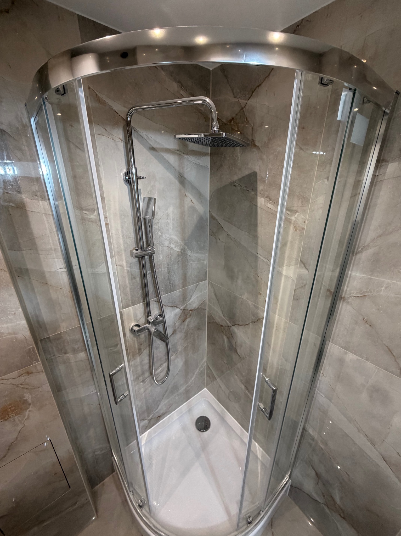 Nowoczesna kabina prysznicowa z deszczownicą, wykończona marmurowymi płytkami w odcieniach szarości i beżu. Chromowane detale podkreślają elegancję.