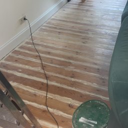 Drewniana podłoga,która ma około 100 lat,została odrestaurowana poprzez przeszlifowanie wierzchniej warstwy drewna co umożliwiło oczyszczenie starej masy szpachlowej i położenie nowej.Nałożenie kilku warstw oleju,co dało efekt wizualny jak i praktyczny.