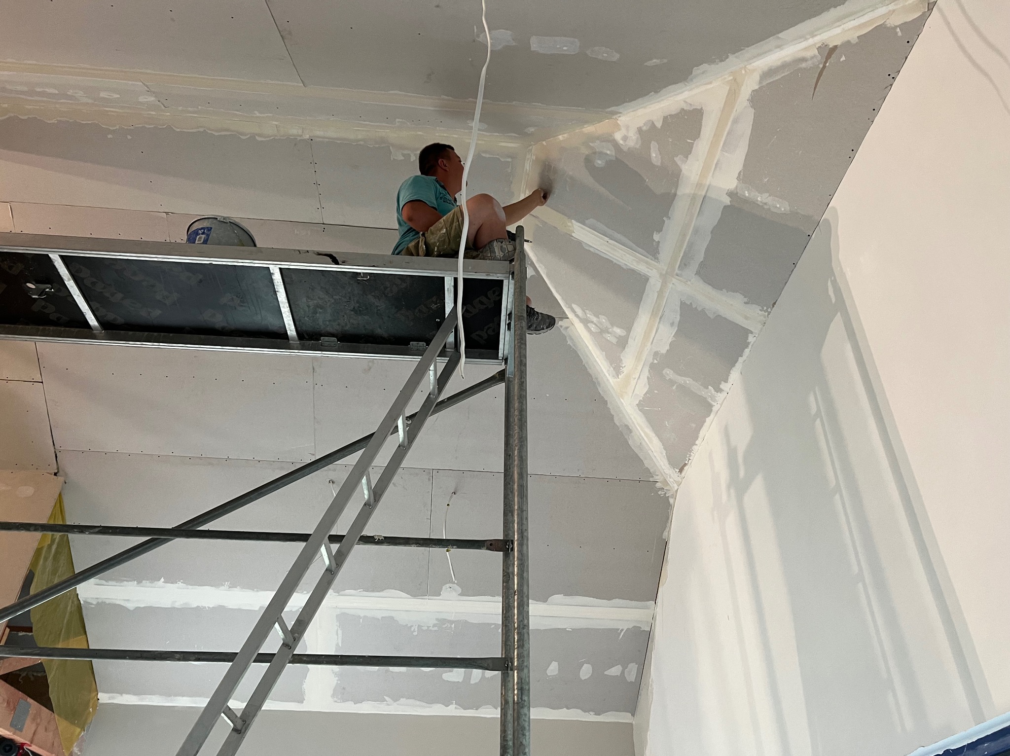 Pracownik na rusztowaniu szpachluje łączenia płyt gipsowo-kartonowych na skośnym suficie poddasza, wykończenie wnętrza.