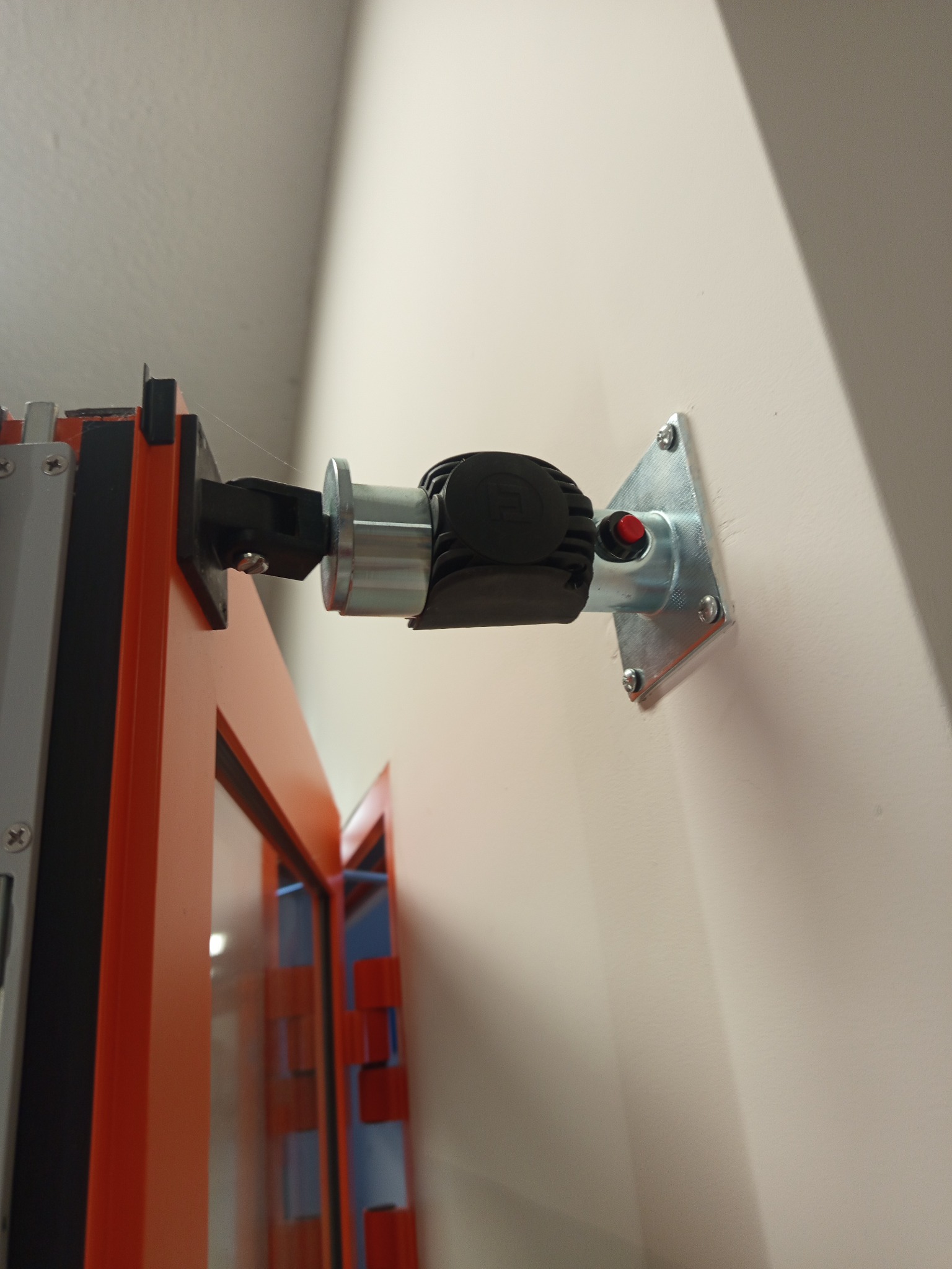 Zamontowany napęd do bramy garażowej z widocznym mocowaniem do ściany i elementami konstrukcyjnymi bramy w kolorze pomarańczowym.
