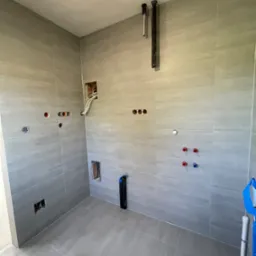 Wykończona płytkami łazienka w Łańcucie. Widoczne wyprowadzone instalacje wodne i elektryczne. Ułożone płytki podłogowe i ścienne w odcieniach szarości.