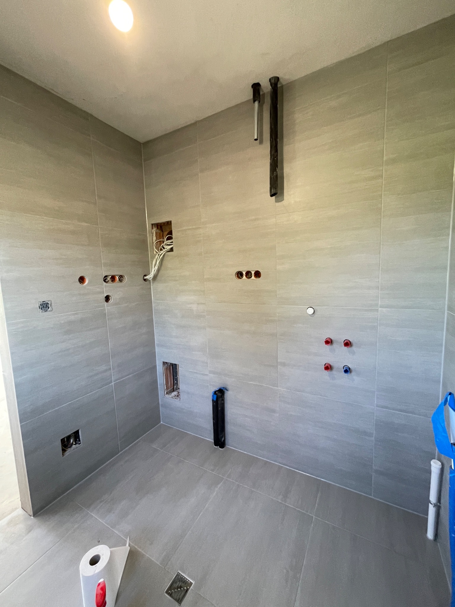 Wykończona płytkami łazienka w Łańcucie. Widoczne wyprowadzone instalacje wodne i elektryczne. Ułożone płytki podłogowe i ścienne w odcieniach szarości.