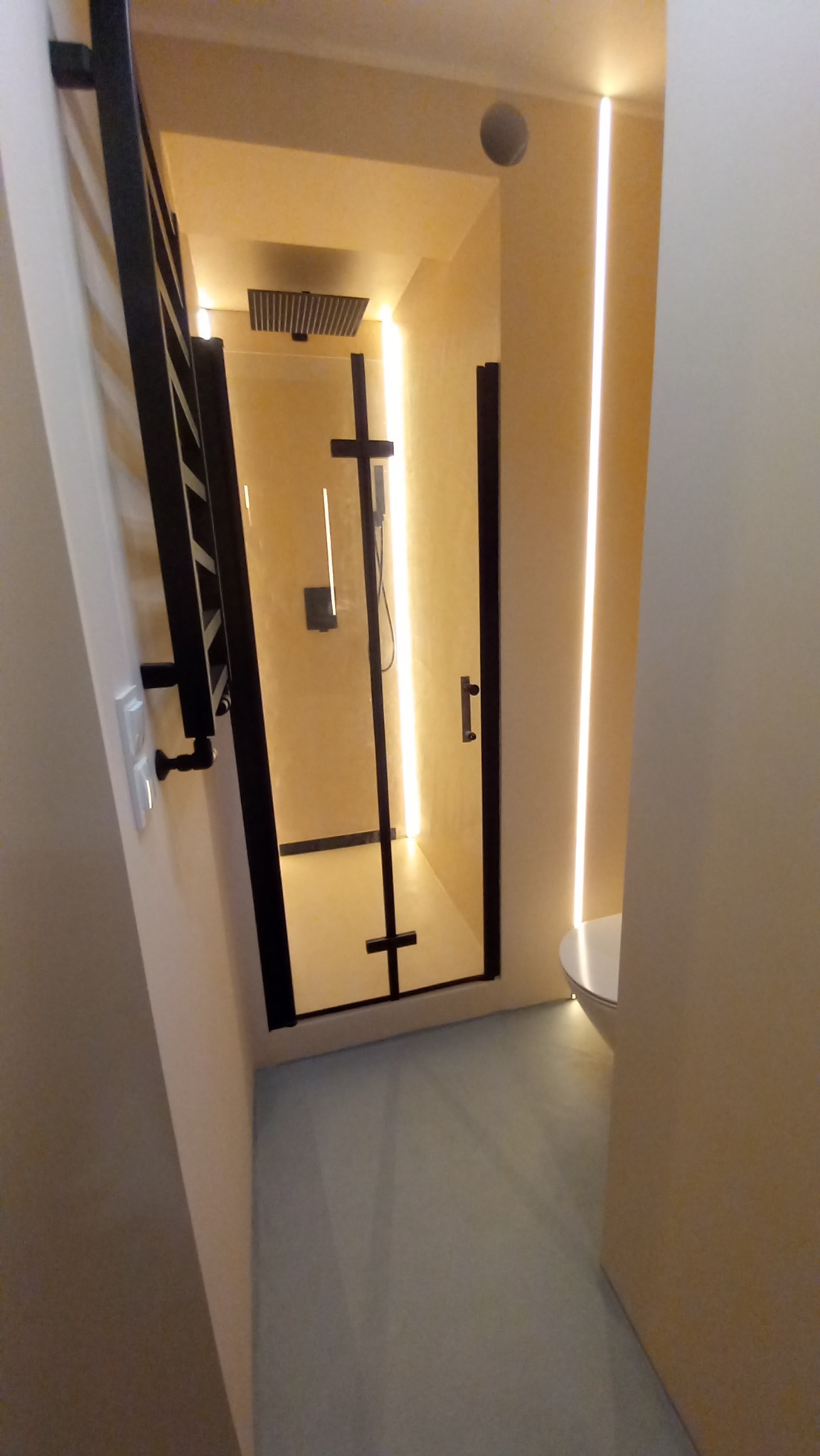 Nowoczesna kabina prysznicowa z czarnymi profilami i deszczownicą, podświetlona pionowymi listwami LED, widok z zewnątrz, z grzejnikiem drabinkowym po lewej stronie.