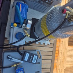 KLIMA DMITRY PETELCZYC - Sprzęt do serwisu klimatyzacji: butla z czynnikiem, pompa próżniowa, waga elektroniczna i manometry na drewnianym podłożu, gotowe do użycia.