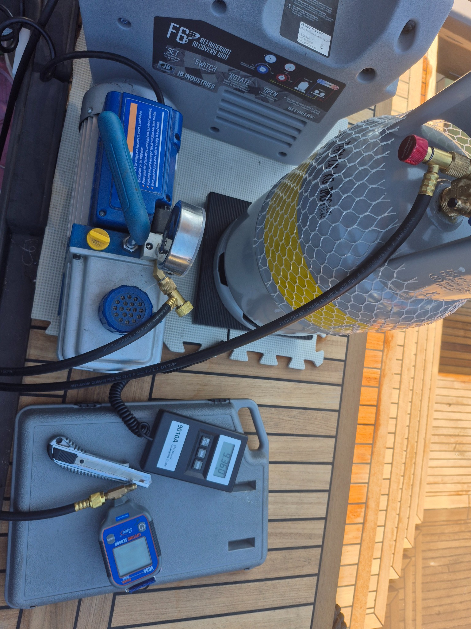 Sprzęt do serwisu klimatyzacji: butla z czynnikiem, pompa próżniowa, waga elektroniczna i manometry na drewnianym podłożu, gotowe do użycia.