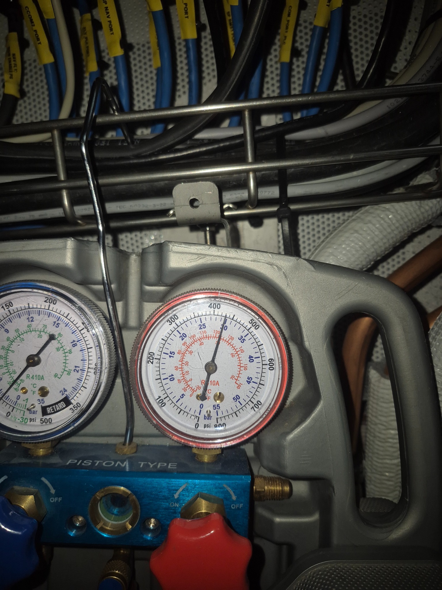 Manometry podłączone do instalacji klimatyzacji, widoczne przewody i kable. Sprzęt serwisowy w trakcie diagnostyki lub naprawy. Bliskie ujęcie na detale.