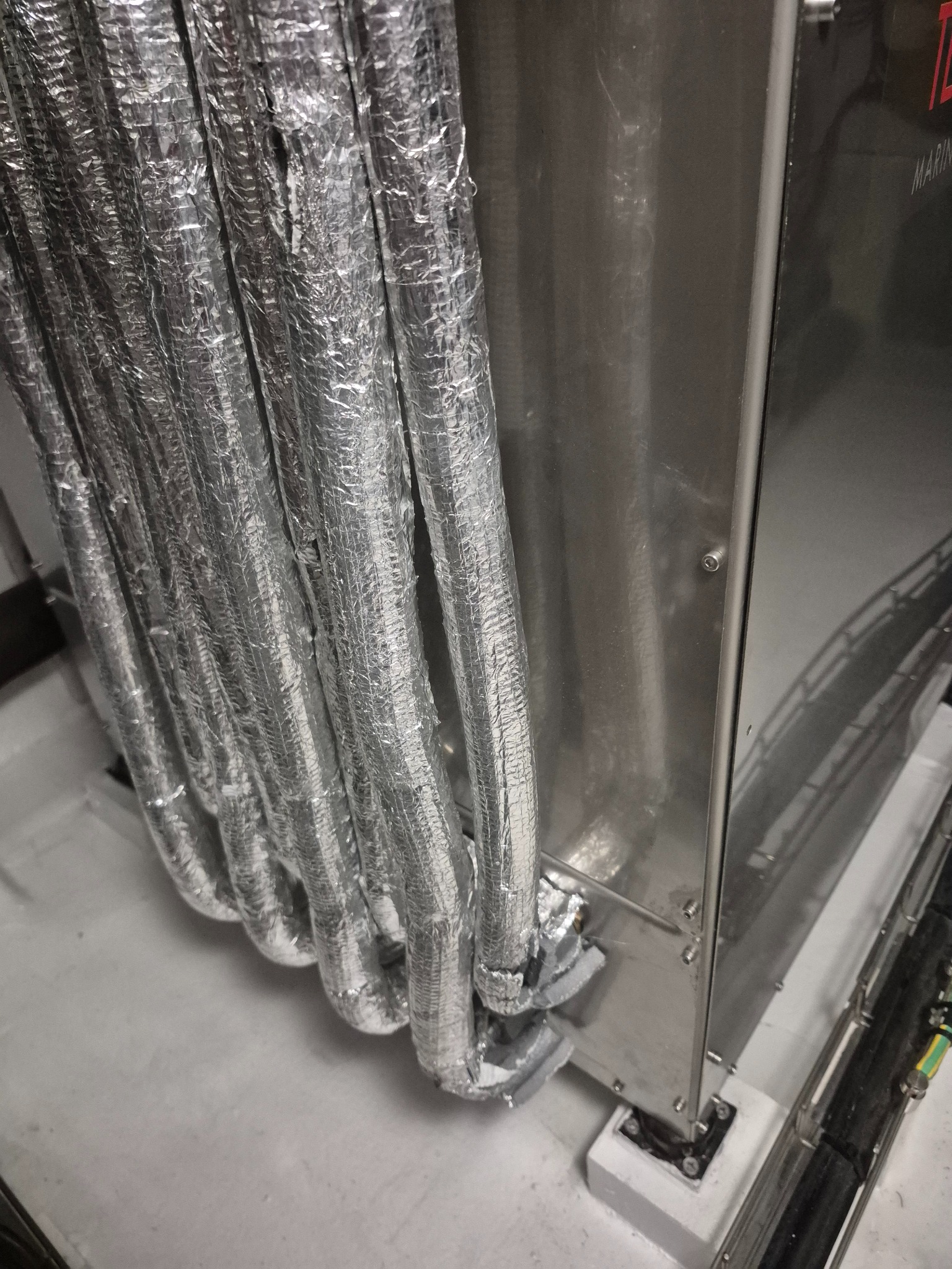 Instalacja klimatyzacji: izolowane rury aluminiową folią, podłączone do metalowej obudowy urządzenia. Widoczne detale mocowania i uszczelnienia.