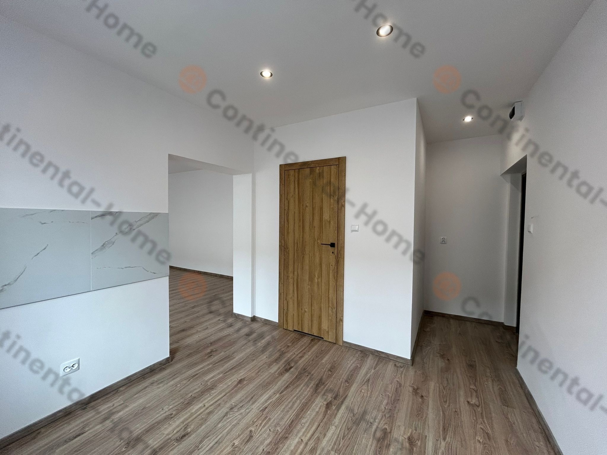 Jasne wnętrze po remoncie z panelami podłogowymi, drewnianymi drzwiami i fragmentem ściany wykończonej płytami imitującymi marmur.