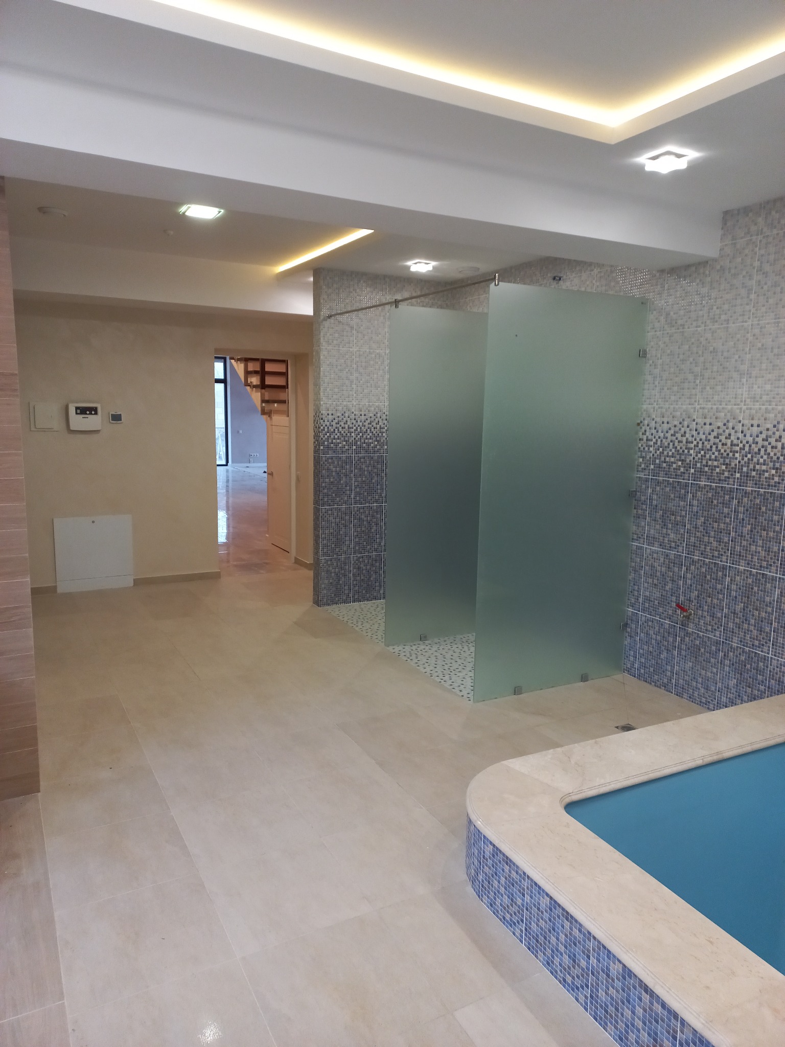 Wykończona łazienka z kabinami prysznicowymi z matowego szkła, mozaiką na ścianach i podłodze oraz fragmentem basenu z mozaikowym wykończeniem.