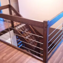 Nowoczesna balustrada z ciemnego drewna i metalowych prętów zabezpieczająca schody, widok z góry na drewnianą podłogę.