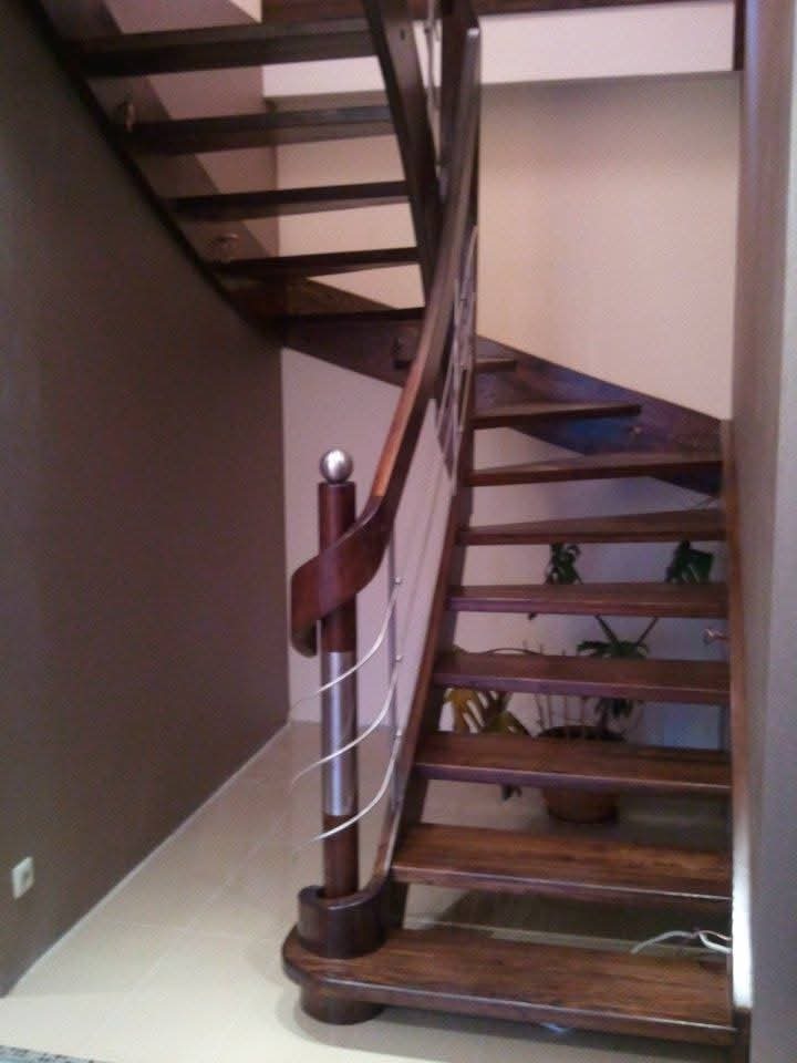 Brązowe schody z drewnianymi stopniami i balustradą z elementami metalowymi, widoczne z dołu.