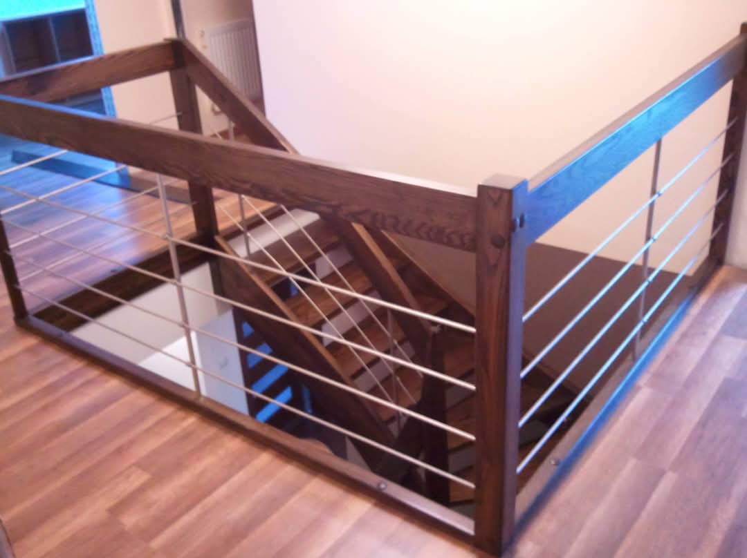 Nowoczesna balustrada z ciemnego drewna i metalowych prętów zabezpieczająca schody, widok z góry na drewnianą podłogę.