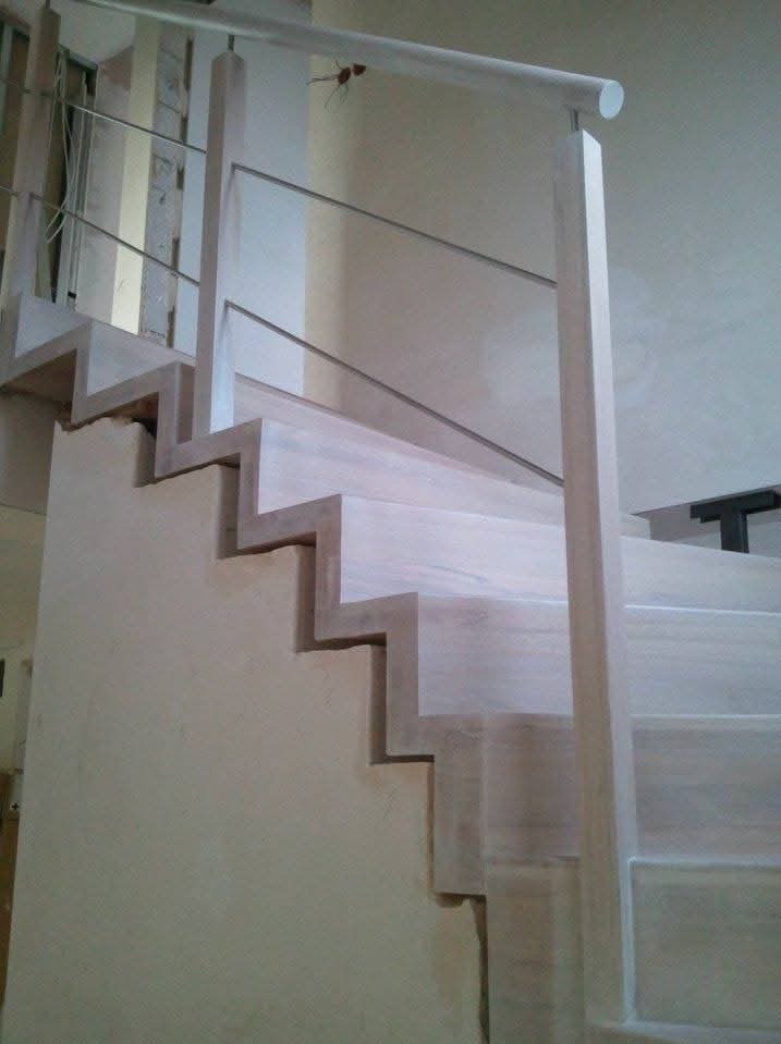 Surowe drewniane schody z metalową balustradą w trakcie montażu, widoczne niedoskonałości wykończenia i elementy konstrukcyjne.