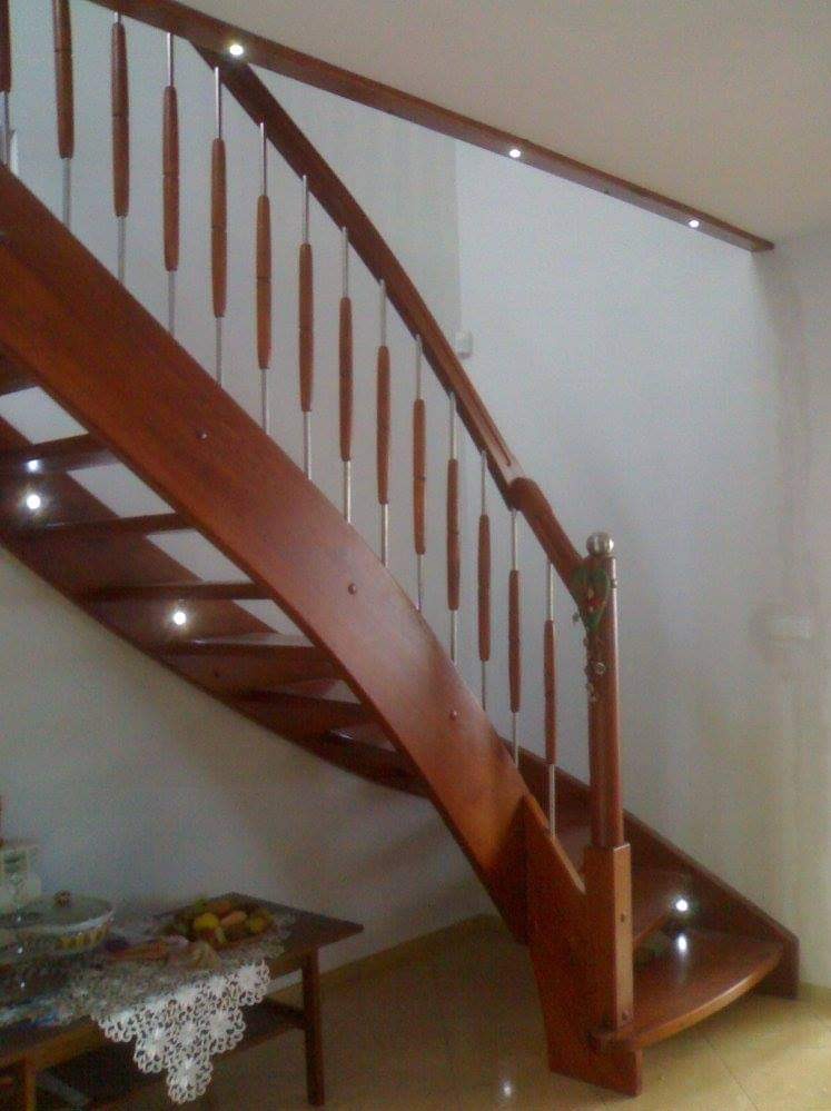 Drewniane schody z balustradą ze stali nierdzewnej i drewnianymi szczeblami, oświetlone punktowo, widok z dołu z fragmentem stołu z owocami.