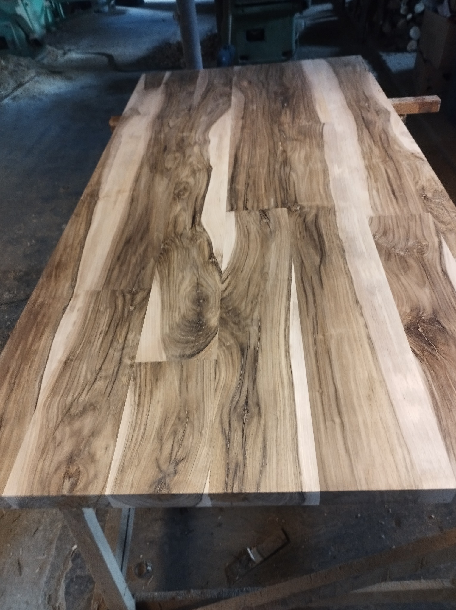 Surowy blat z klejonego drewna o wyraźnym usłojeniu, widoczne niedoskonałości obróbki, umieszczony na roboczym stole w warsztacie.