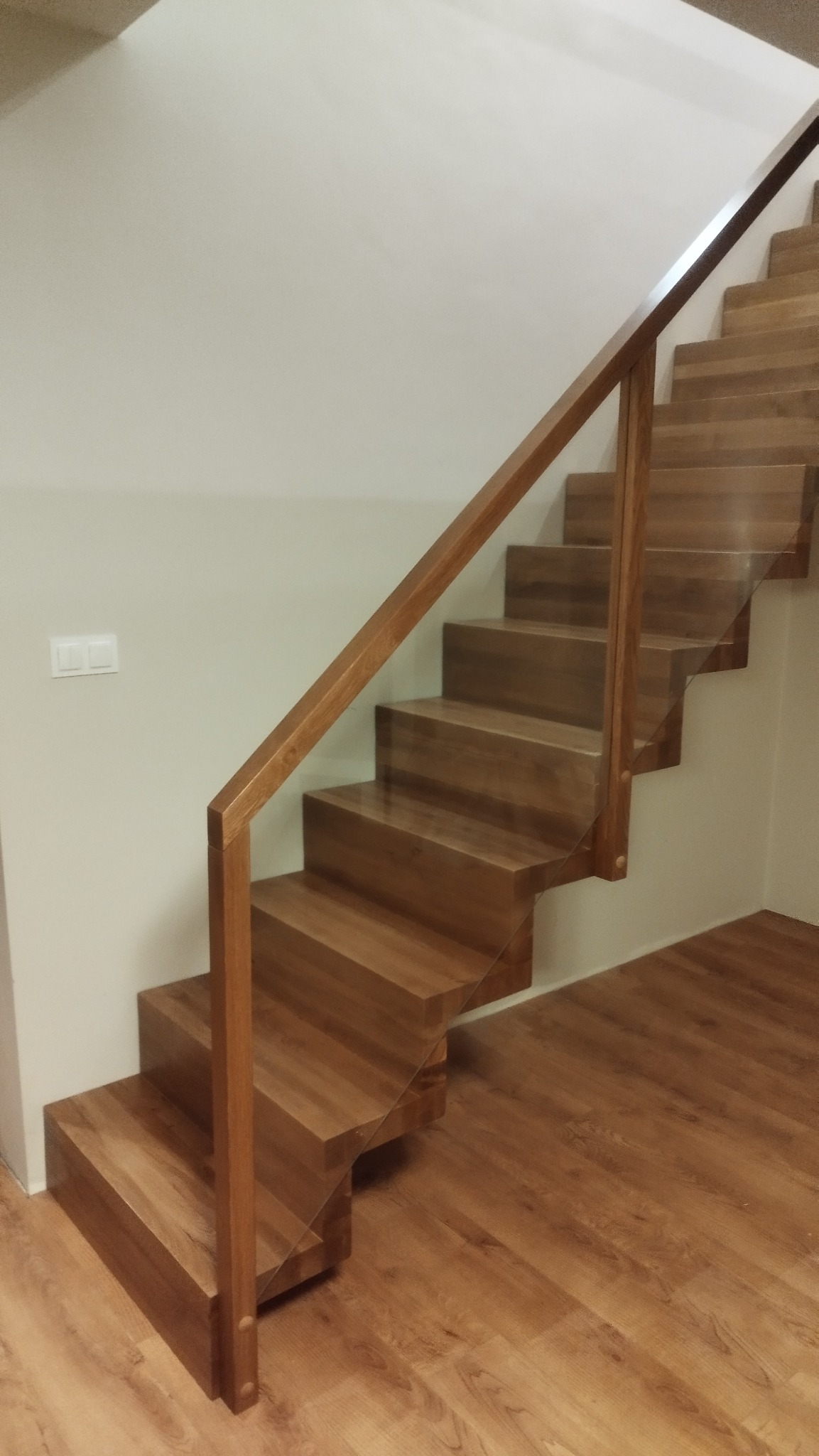 Nowoczesne, drewniane schody z przeszkloną balustradą w Bobolicach. Naturalne oświetlenie podkreśla ciepły odcień drewna i minimalistyczny design.