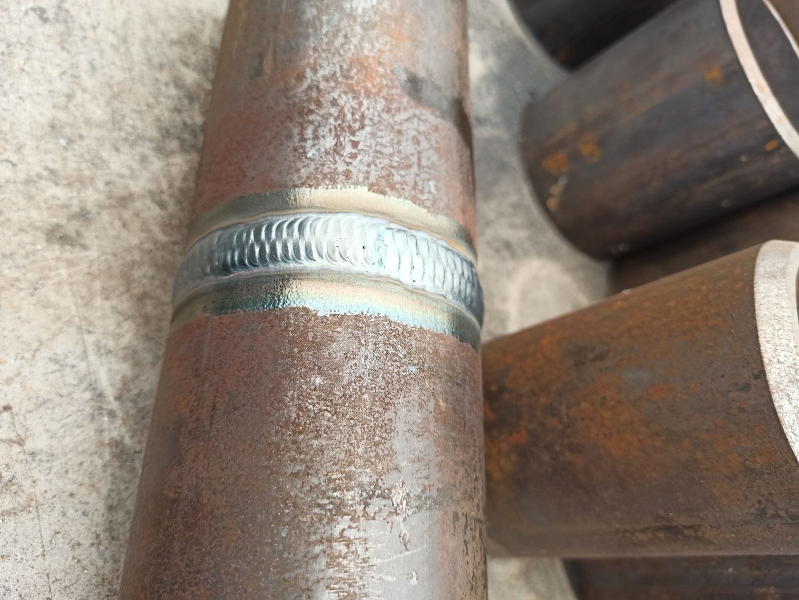 Spoina spawalnicza na rurze stalowej, widoczne ślady korozji na powierzchni metalu i charakterystyczny wzór spawu.