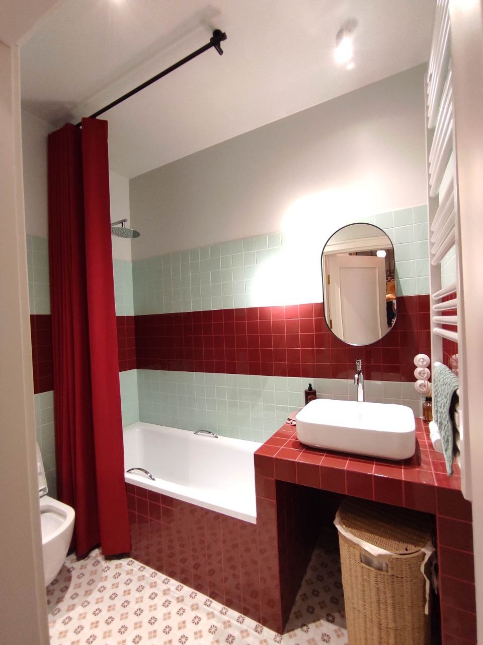 Wykończona łazienka z czerwono-białymi płytkami, białą wanną i umywalką nablatową, zasłoną prysznicową i dekoracyjną podłogą.