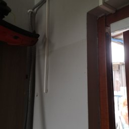 PRO-Elektro Serhii Kopylov - Szara rura karbowana i biała listwa przymocowane do ściany w pobliżu framugi drzwi, widoczne elementy instalacji elektrycznej.